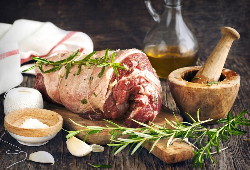 Raw leg of lamb on a table with herbs, salt, onion, and a pestle and mortar Raw leg of lamb on a table with herbs, salt, onion, and a pestle and mortar