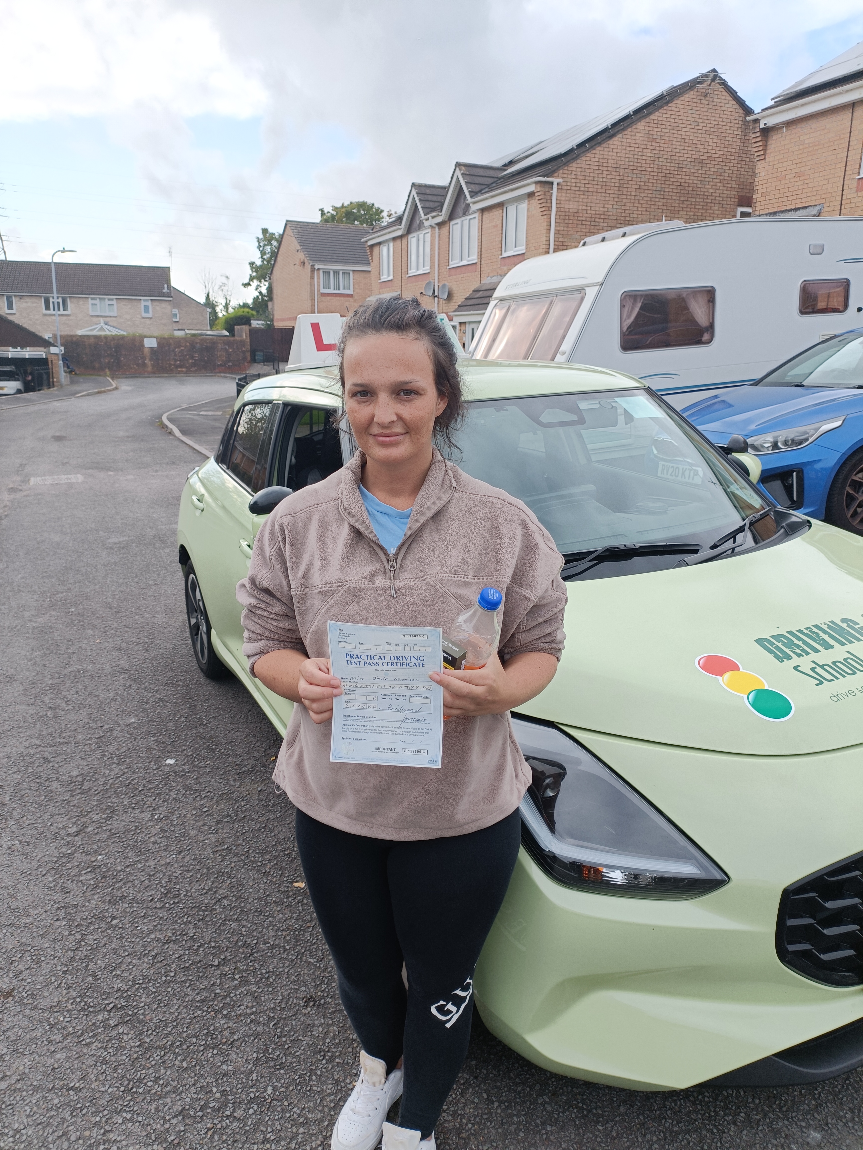 “Learner driver smiling and holding a driving test pass certificate beside the car “Learner driver smiling and holding a driving test pass certificate beside the car