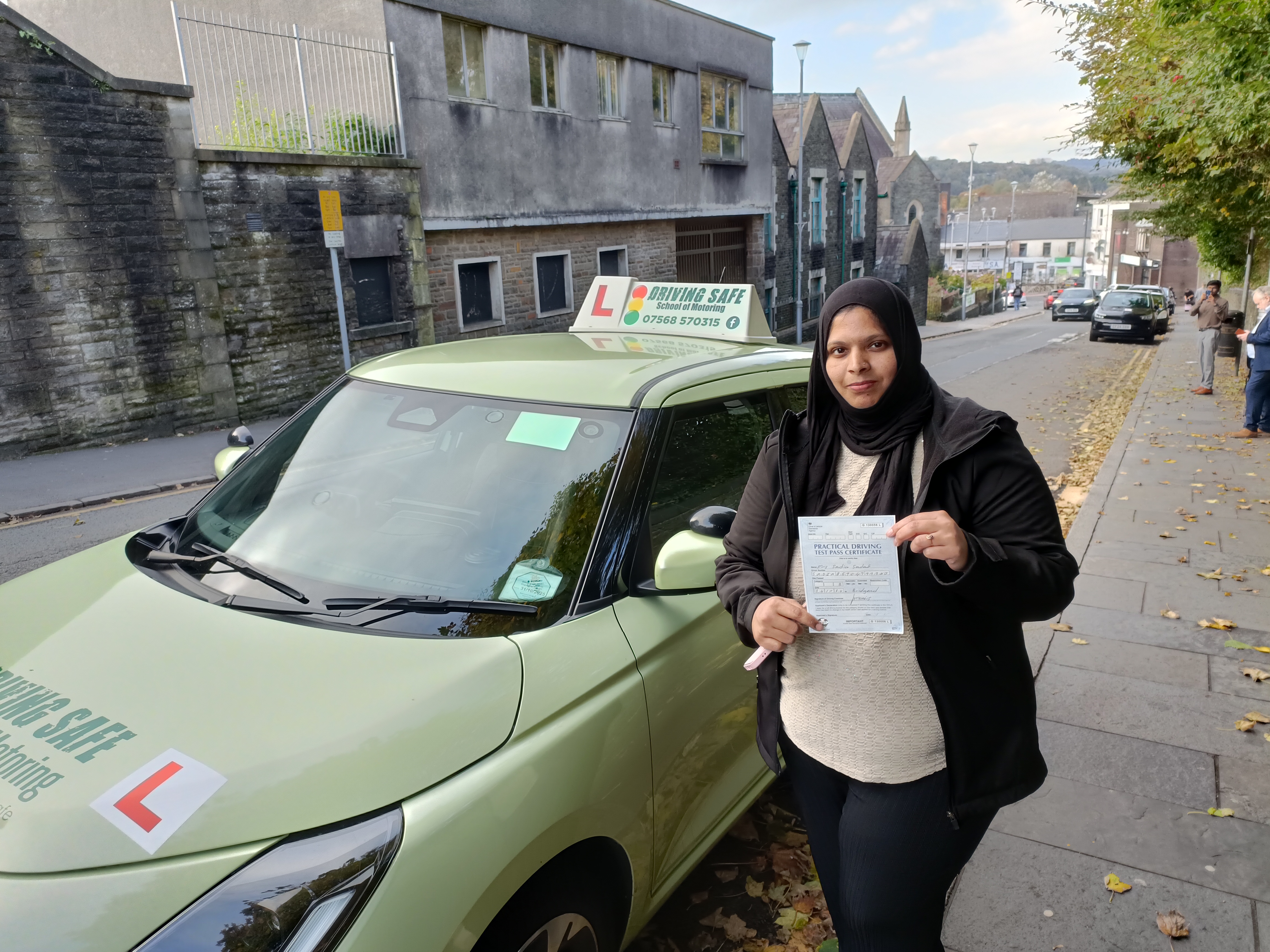 Learner driver smiling and holding a driving test pass certificate beside a driving school car Learner driver smiling and holding a driving test pass certificate beside a driving school car