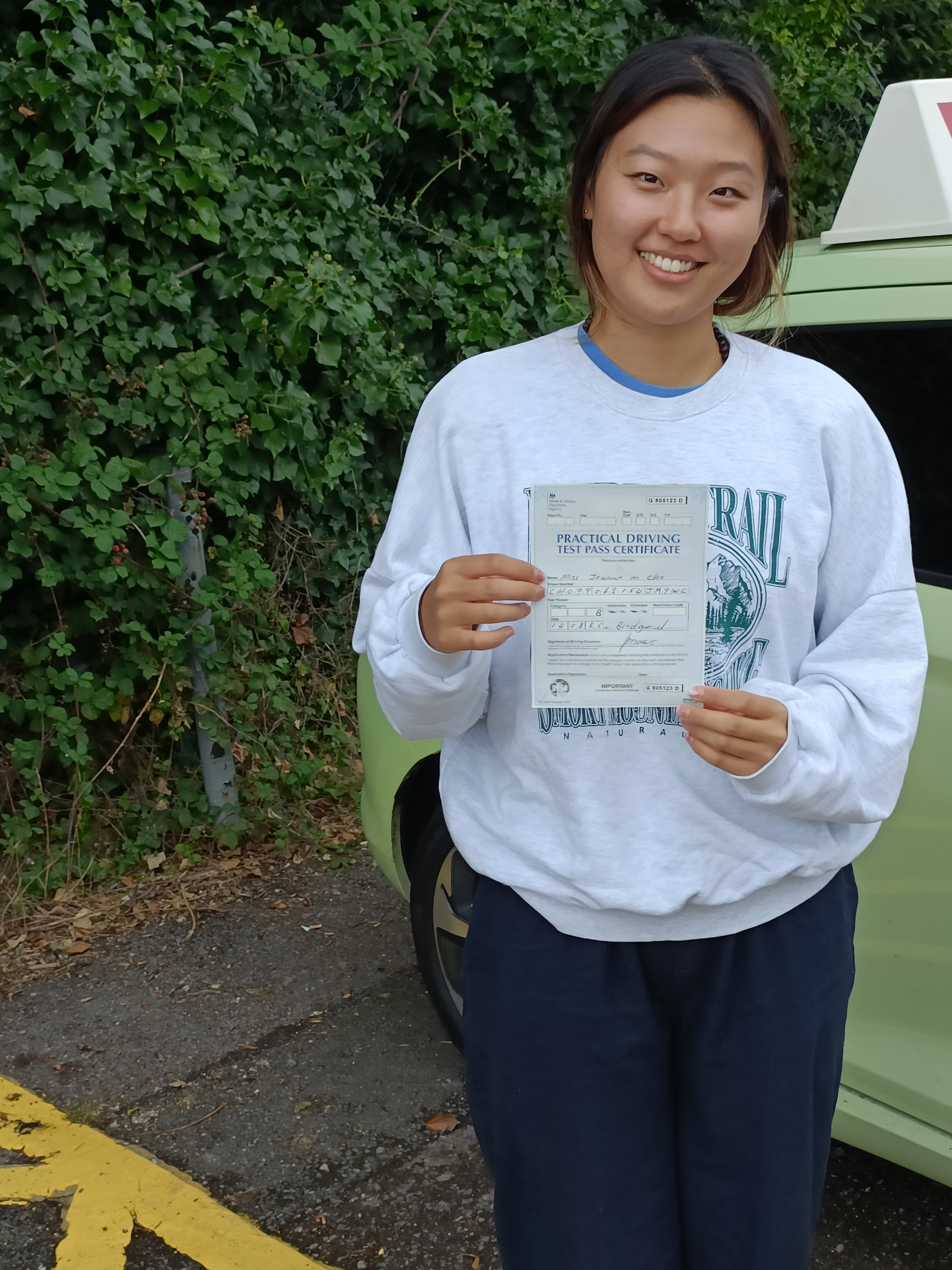 Female learner driver smiling and holding her driving test pass certificate beside the Driving Safe School of Motoring training vehicle in Bridgend Female learner driver smiling and holding her driving test pass certificate beside the Driving Safe School of Motoring training vehicle in Bridgend