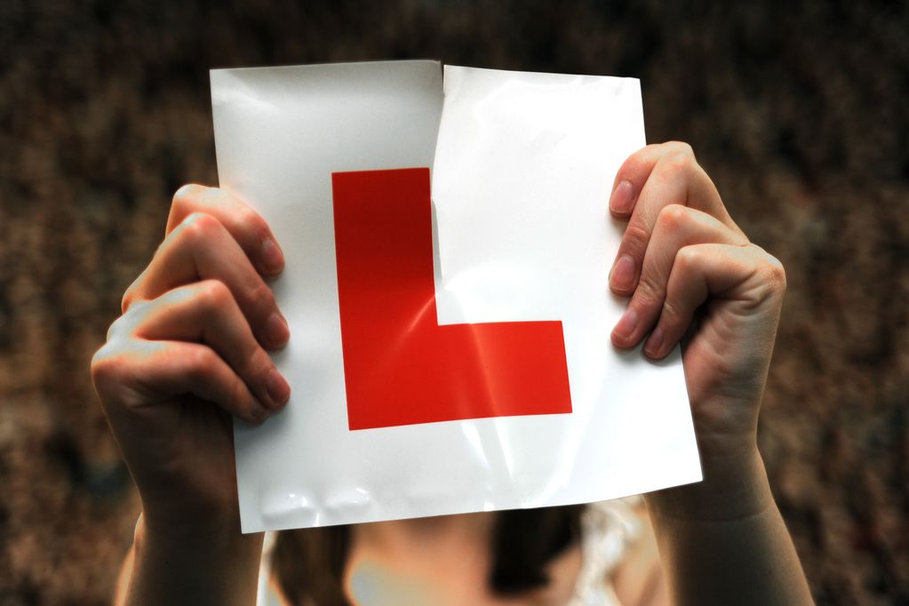 Female learner driver holding and tearing an L‑plate in a celebratory pose Female learner driver holding and tearing an L‑plate in a celebratory pose